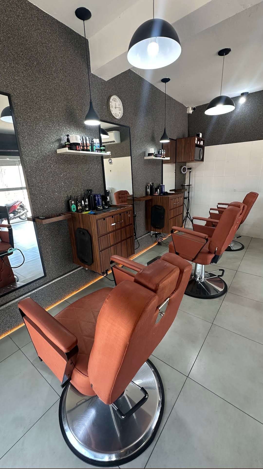 Interior da Trimmos Barbearia, com cadeiras de couro caramelo enfileiradas, bancadas de madeira, espelhos e parede cinza