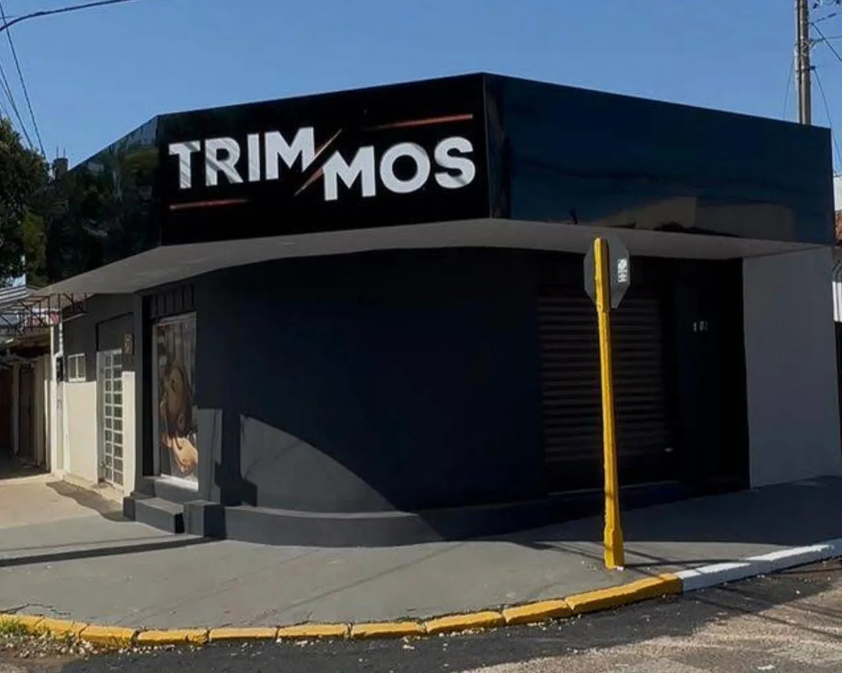 Fachada preta da Trimmos Barbearia, com o letreiro TRIMMOS, na esquina